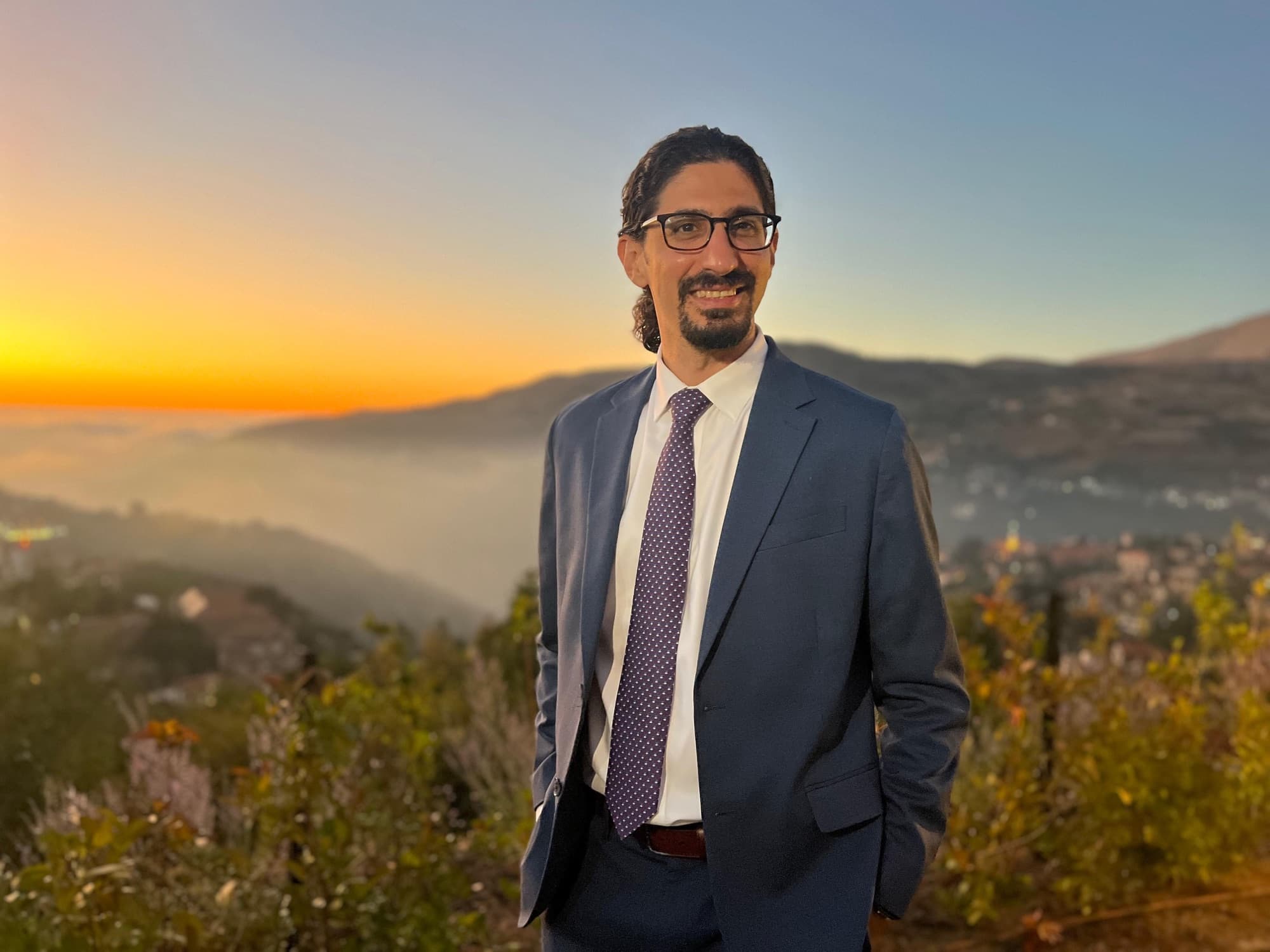 Carlo Mahfouz in a suit at sunset above the hills